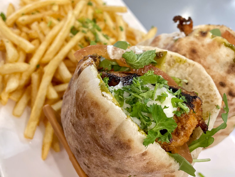 Closeup photo of a pita sandwich and french fries from the Dar menu: CHICKEN TAWOOK PITA grilled chicken thigh, garlic sauce, red onion, arugula mint, tomatoes, pickles